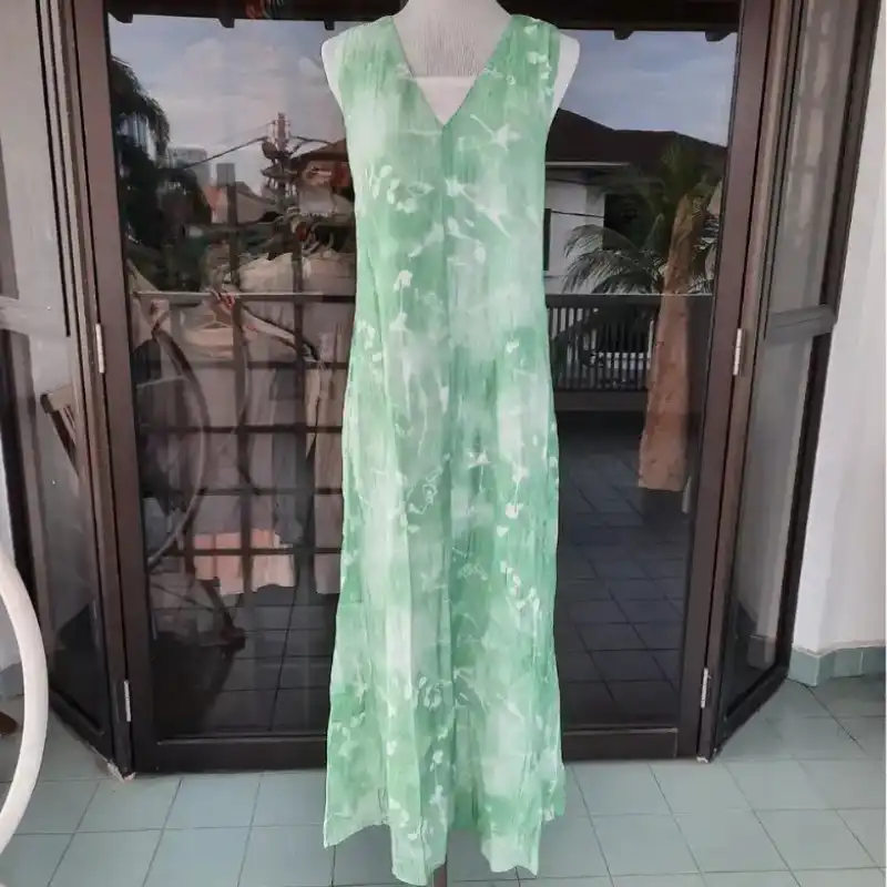 Green sleeveless dress photographed at home in front of cluttered balcony doors