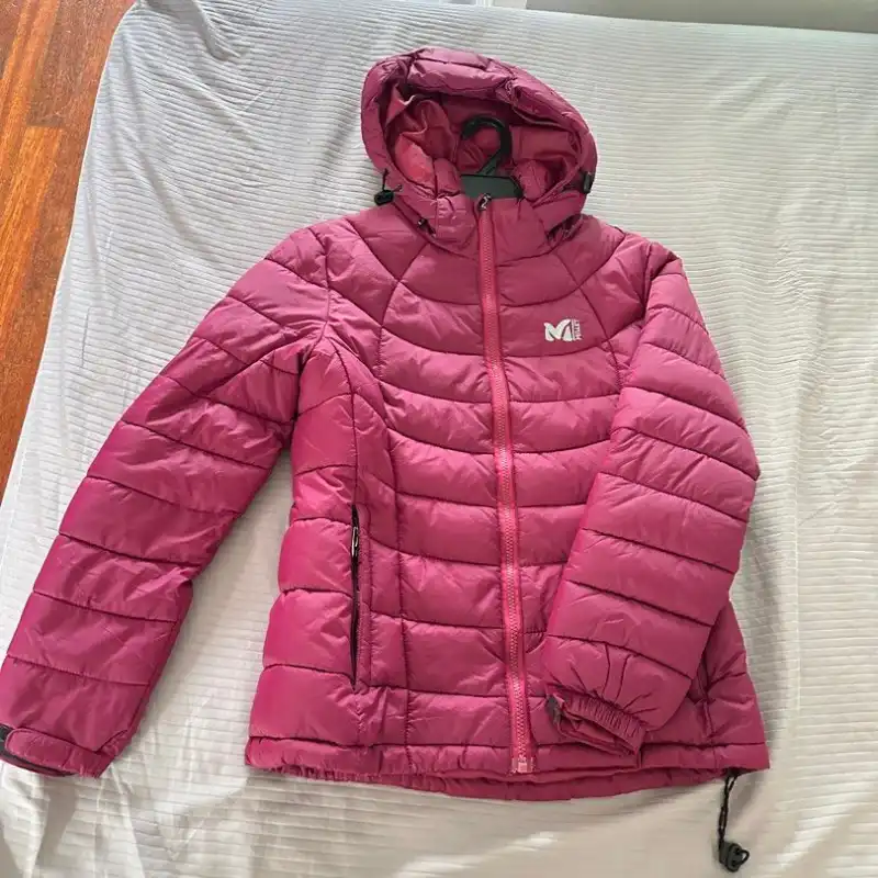 Pink Millet puffer jacket laid flat on a bed showing wrinkled, shapeless presentation
